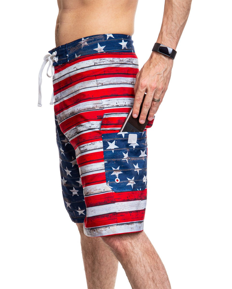 Men's USA Flag Distressed Boardshorts- Barnboard Side View With Man Putting Phone In Side Pocket